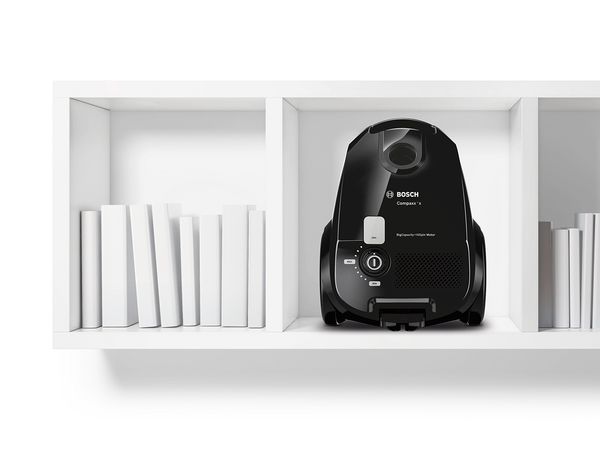 Small and sleek bagged vacuum in black tucked into an open, low-hanging shelf
