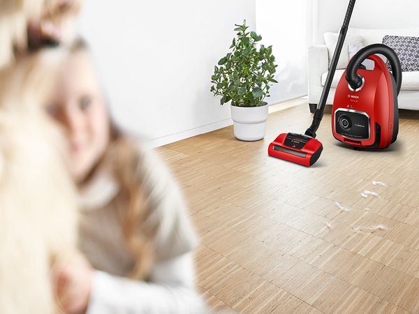 Girl hugging a shaggy dog with a ProAnimal vacuum ready to suck up hair from a hardwood floor in the background