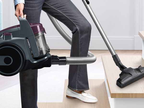 Woman holding a compact, black bagless vacuum as she cleans the stairs