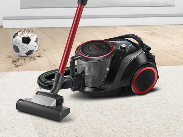 Bosch ProPower vacuum on a living room rug next to a football covered in dirt and sand 