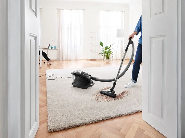 Wing doors opening into a spacious living room with a Bosch bagless vacuum picking up dirt on a high-pile rug