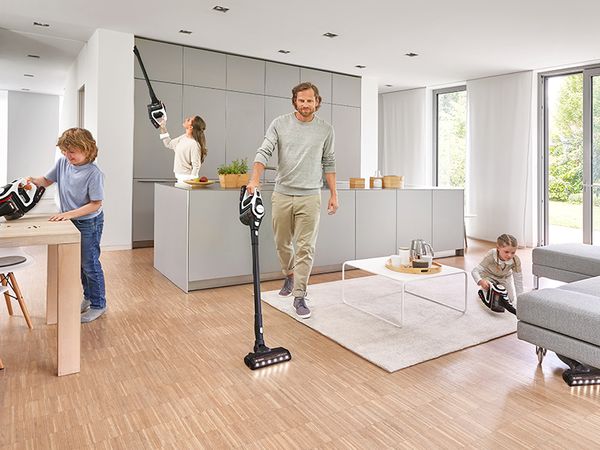Young family vacuuming hard-to-reach spots in their living room with handheld cordless vacuums