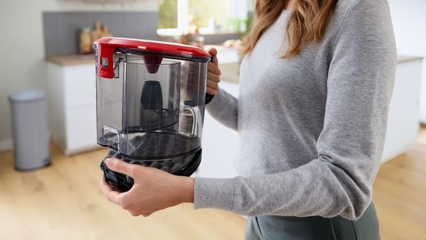 A woman lifts the dust box out from a canister vacuum cleaner.