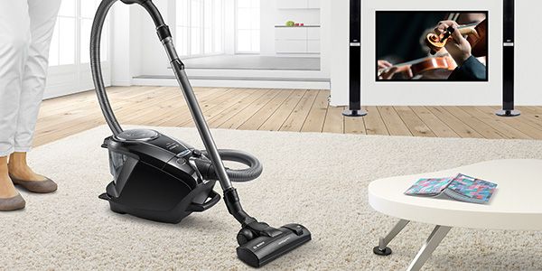 Black bagless vacuum cleaner cleaning up on a beige rug