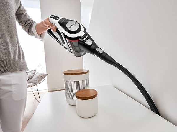 Person vacuums behind sideboard with Unlimited hand-held with the long, flexible crevice nozzle attachment