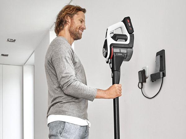 Man hangs Unlimited cordless vacuum on the wall docking station to charge.