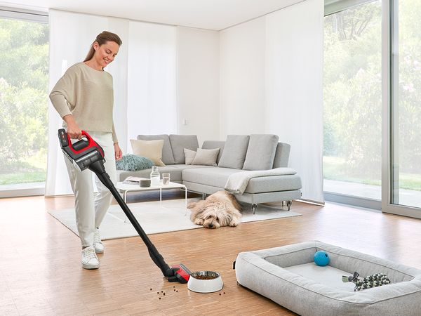 Woman vacuuming spilled dog food with Unlimited ProAnimal next to a shaggy dog