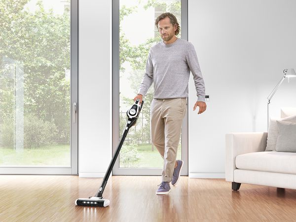 Ein Mann saugt den Hartholzboden eines hellen, geräumigen Wohnzimmers mit einem Unlimited ProParquet.
