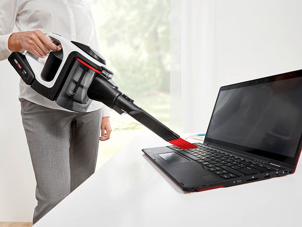 Eine Frau saugt die Tastatur eines Laptops mit einer Düse ab.