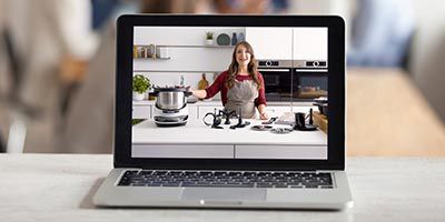 Auf einem Tisch steht ein Laptop. Am Laptop Screen ist eine Frau zu sehen, die den Cookit über Video Chat erklärt.
