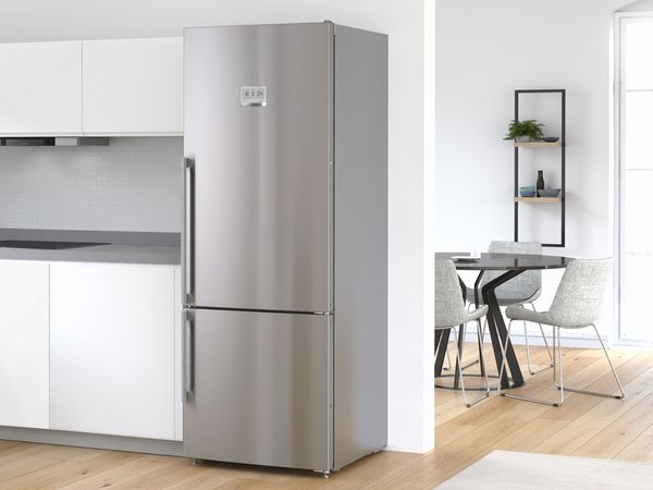 Réfrigérateur-surgélateur pose-libre argent Bosch dans une cuisine blanche moderne, avec la salle à manger en arrière-plan