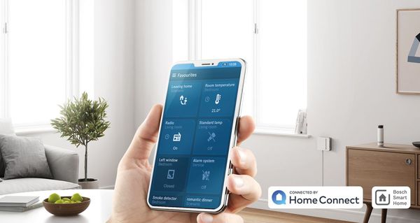 Modern möbliertes Wohnzimmer, im Vordergrund ein Smartphone mit Steuerung für das intelligente Zuhause als Symbol für die Fernsteuerungsfunktionen von Home Connect. 