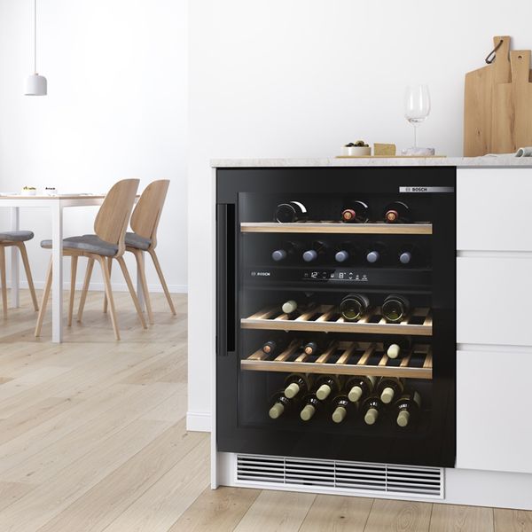 Built-in wine cooler with LED lighting integrated in modern oak cabinetry in a minimalist kitchen with exposed concrete floors