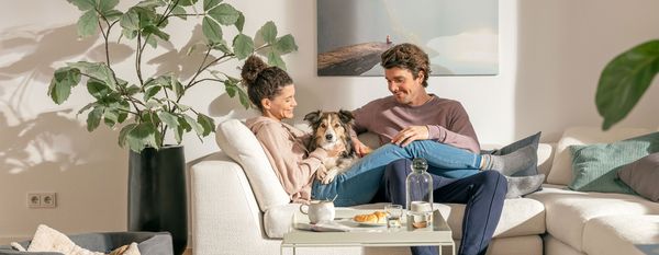 A woman and a man are sitting on a sofa with a dog between them