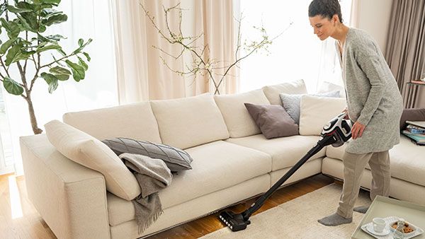 Donna che pulisce lo spazio sotto un divano con un aspirapolvere senza filo Unlimited