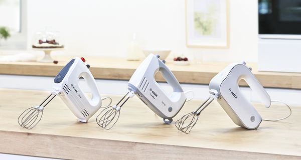 Lineup of three Bosch hand mixers on a wood kitchen worktop.