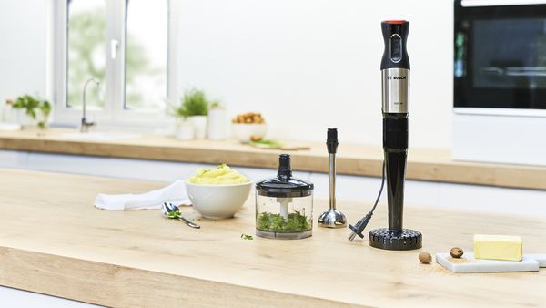 ErgoMixx hand blender with a masher attachment next to other attachments and mashed potatoes.