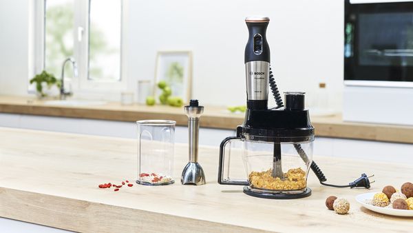Food processor attachment on a MaxoMixx hand blender next to other attachments and energy balls.