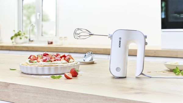 Styline hand mixer with beaters on kitchen worktop next to whipped cream and raspberry cake.