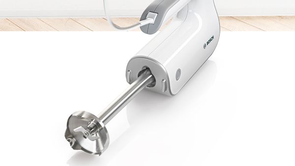 A Bosch hand mixer on its side with a blending shaft attachment.