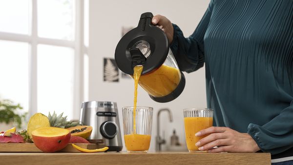 Une personne verse un smoothie à la papaye, mangue et ananas fraîchement concocté dans deux verres.