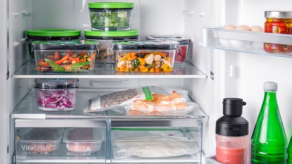 Un réfrigérateur plein d'aliments frais et cuits conditionnés sous vide dans des boîtes de conservation et des sacs.