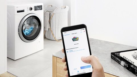 A person checking the washing machine using a smartphone with Home Connect app