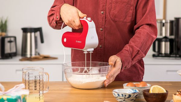 A person in a red shirt whipping cream with a red Styline hand mixer.
