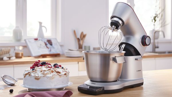 Bosch OptiMUM stand mixer with a whisk next to a delicious-looking cake.
