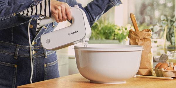 A Bosch hand mixer being used to beat something in a white bowl.