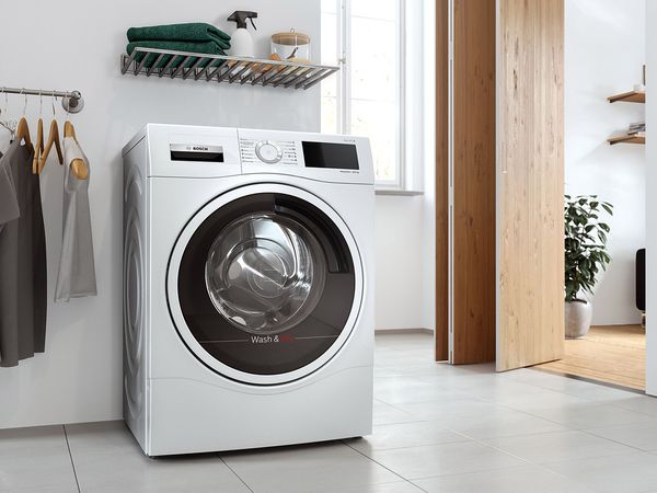 Vaske-/tørremaskine i et åbent vasketum ved siden af en stativ med skjorter.