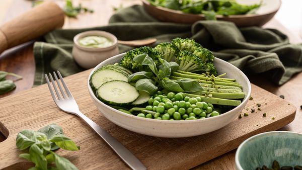 Ciotola di insalata con cetrioli, piselli, broccoli, basilico e condimento a base di avocado.