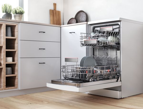Freestanding slimline dishwasher with an open door in a stylish kitchen.