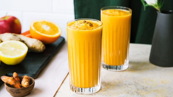 Due bicchieri di succo di frutta giallo con carote, arance, mele e zenzero.