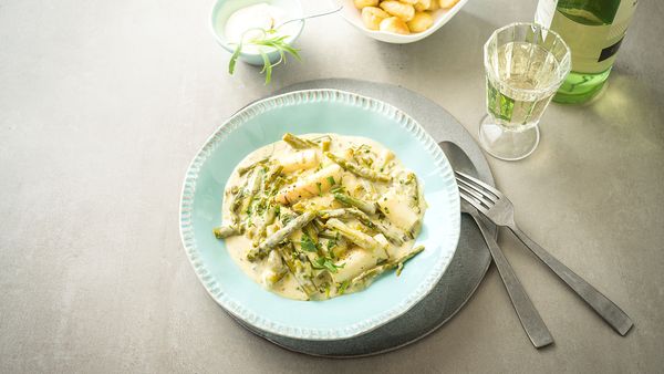Un piatto di verdure cotte con asparagi verdi e bianchi, su un tavolo con vino e contorni.