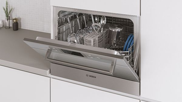 An integrated compact dishwasher in modern kitchenette with a slightly opened door.