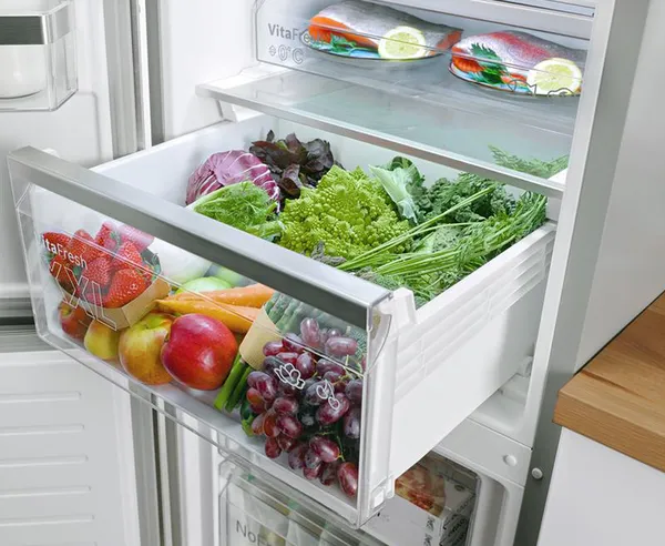 Cassetto del frigorifero aperto con frutta e verdura fresca, tra cui kiwi, uva, mele e lattuga.