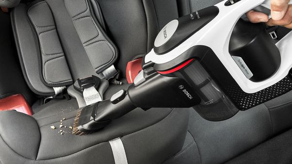 Der Unlimited Akku-Staubsauger mit 2in1 Möbelpinsel und Polsterdüse saugt Krümel vom Autositz.