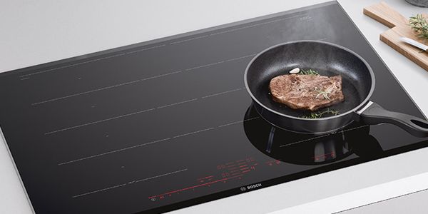 Uma grande placa de indução com uma frigideira a cozinhar um bife.