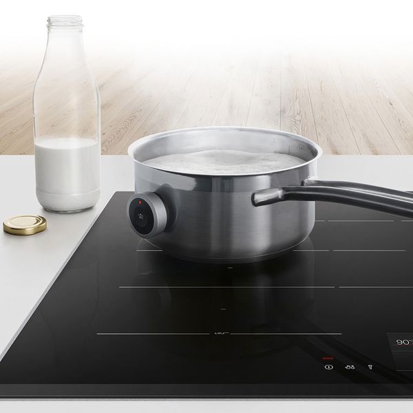 A cooktop with a pot of boiling milk and a jug of milk next to it.
