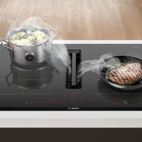 Une casserole et une poêle chaude sur une table à induction qui aspire la vapeur.