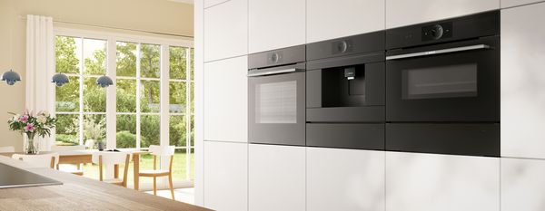 Oven konveksi Bosch di latar depan ruang makan modern yang terang.