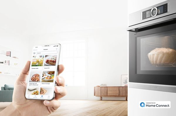 Home Connect appen på en smartphone. En smart ovn i baggrunden.