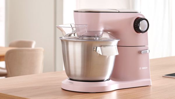 Küchenmaschine mit rosafarbenem Gehäuse und Edelstahl-Rührschüssel.