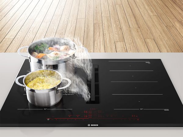 Une table de cuisson à hotte intégrée avec des casseroles dans lesquelles cuisent des aliments pendant que la hotte aspire la vapeur.