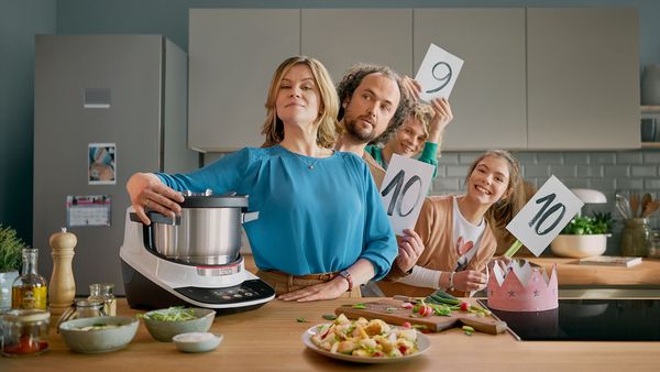 Eine Familie steht an der Kücheninsel und vergibt mit Schildern Höchstnoten für den Bosch Cookit, der auf der Arbeitsplatte steht.