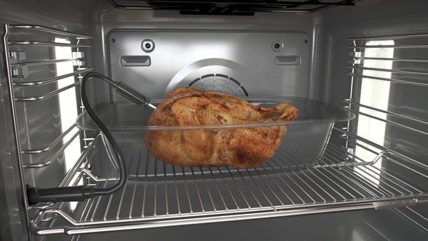 A whole roast chicken with a meat thermometer cooking in a Bosch oven.