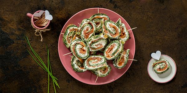A Cookit recipe for finger food: festive cream cheese and salmon rolls served in slices on a colourful plate with toothpicks.  