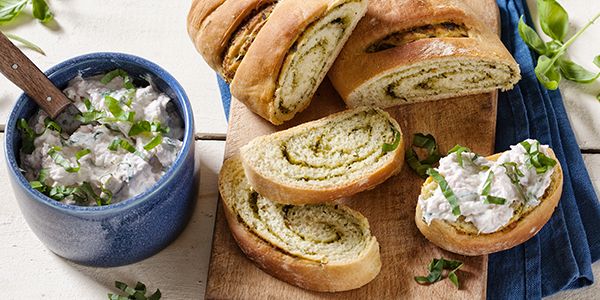 Pesto bread, a Cookit recipe, being sliced and topped with cream cheese and herbs.   