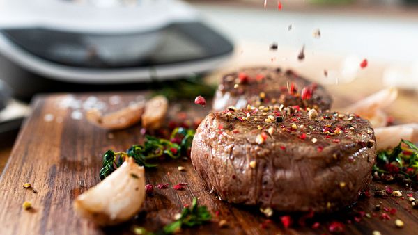 Perfekt gebräuntes Steak, garniert mit frisch geriebenen Pfefferkörnern, mit dem Cookit im Hintergrund.